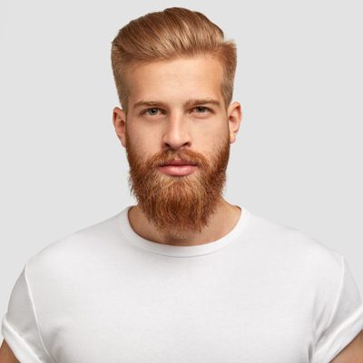 Headshot of red haired serious young male blogger looks confidently at camera, thinks about new content of his web page, dressed casually, earns money distantly, isolated over white background